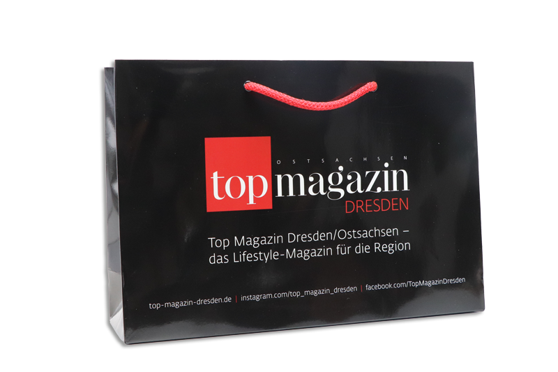 Luxuspappiertasche für das Topmagazin, vollflächig schwarz mit rot weißem Logo und roter Tragekordel